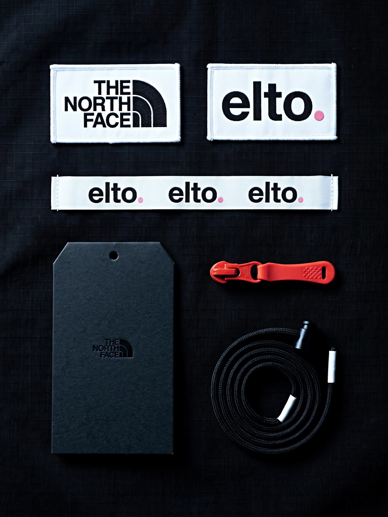 Label system on black: woven The North Face and elto. labels, a hang tag, a zip puller and a drawcord
