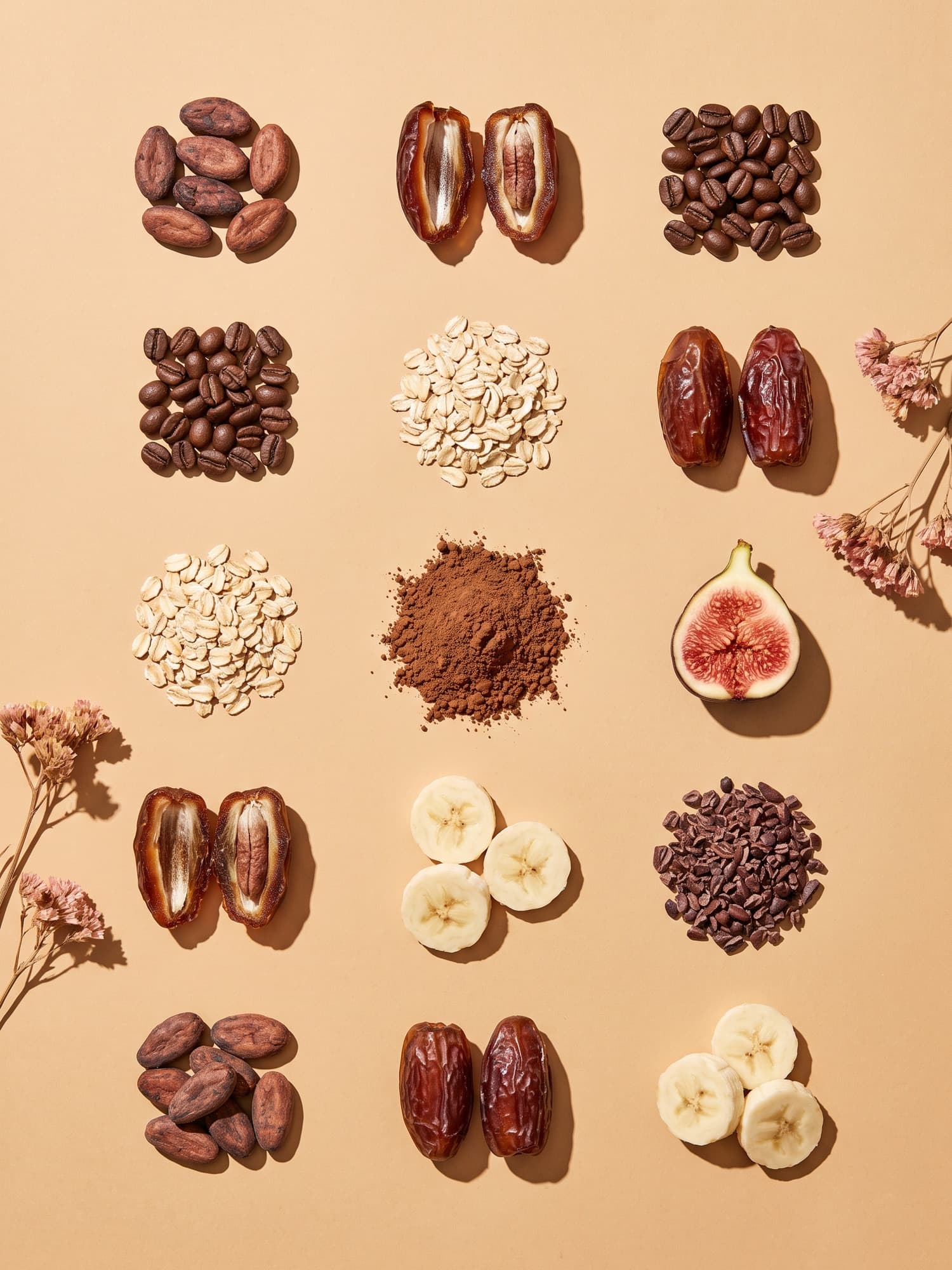 Ingredients laid out in a grid on a sand background: cacao beans, dates, coffee, oats, figs and banana
