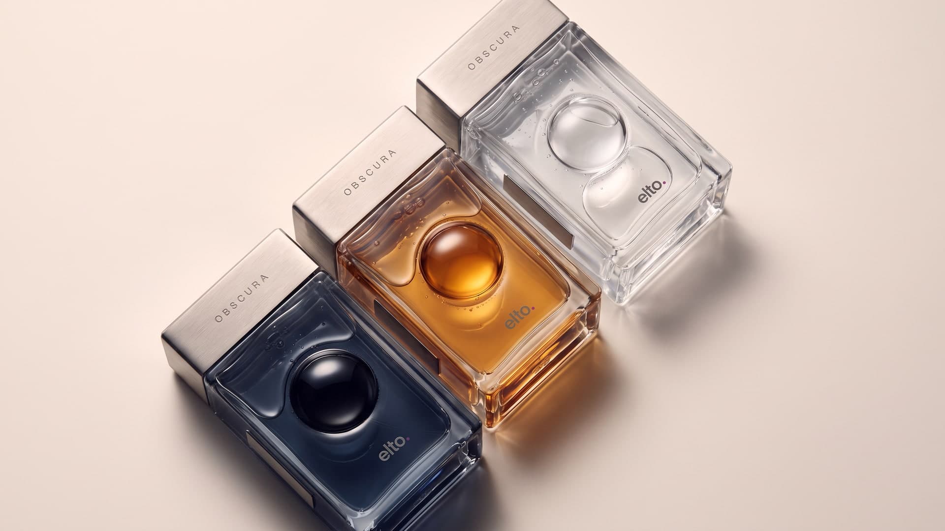 The three bottles, navy, amber and clear, lying in a diagonal line on cream, seen from above